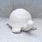 Handmade unpainted ceramic turtle on a lacy ecru table cloth and a curtain behind it.  It is facing slightly toward the left.